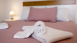 Un lit bien fait, avec une couvre-lit rose, un oreiller blanc et une serviette blanche roulée posée sur le lit.