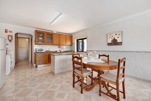Une cuisine avec des meubles de rangement en bois, une table à manger avec des chaises, un four à micro-ondes et un évier.