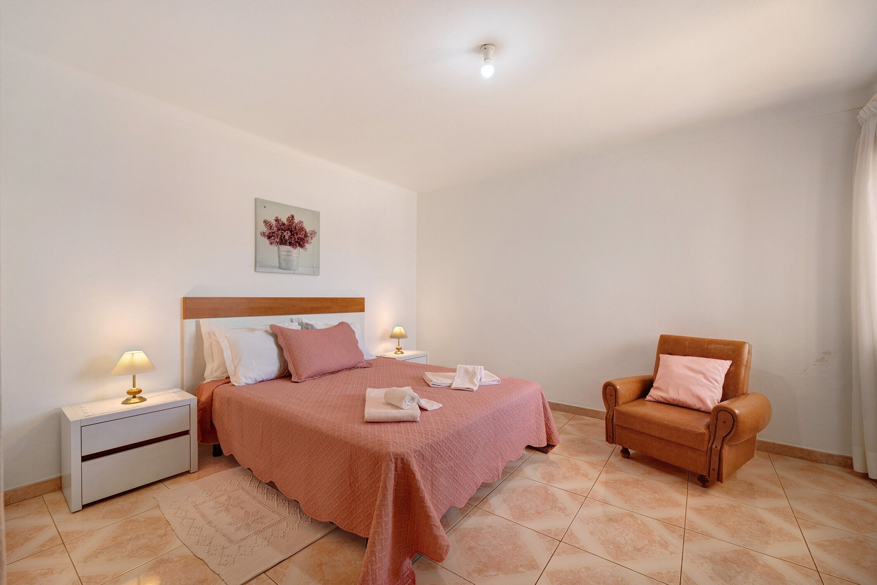 Une chambre à coucher comprenant un lit, une table de chevet, une chaise et un tableau accroché au mur.