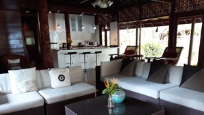 A modern living room with a sectional sofa, a glass coffee table, and a kitchen area in the background.