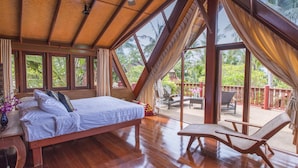 A spacious room with a large bed, wooden flooring, and a balcony with seating.