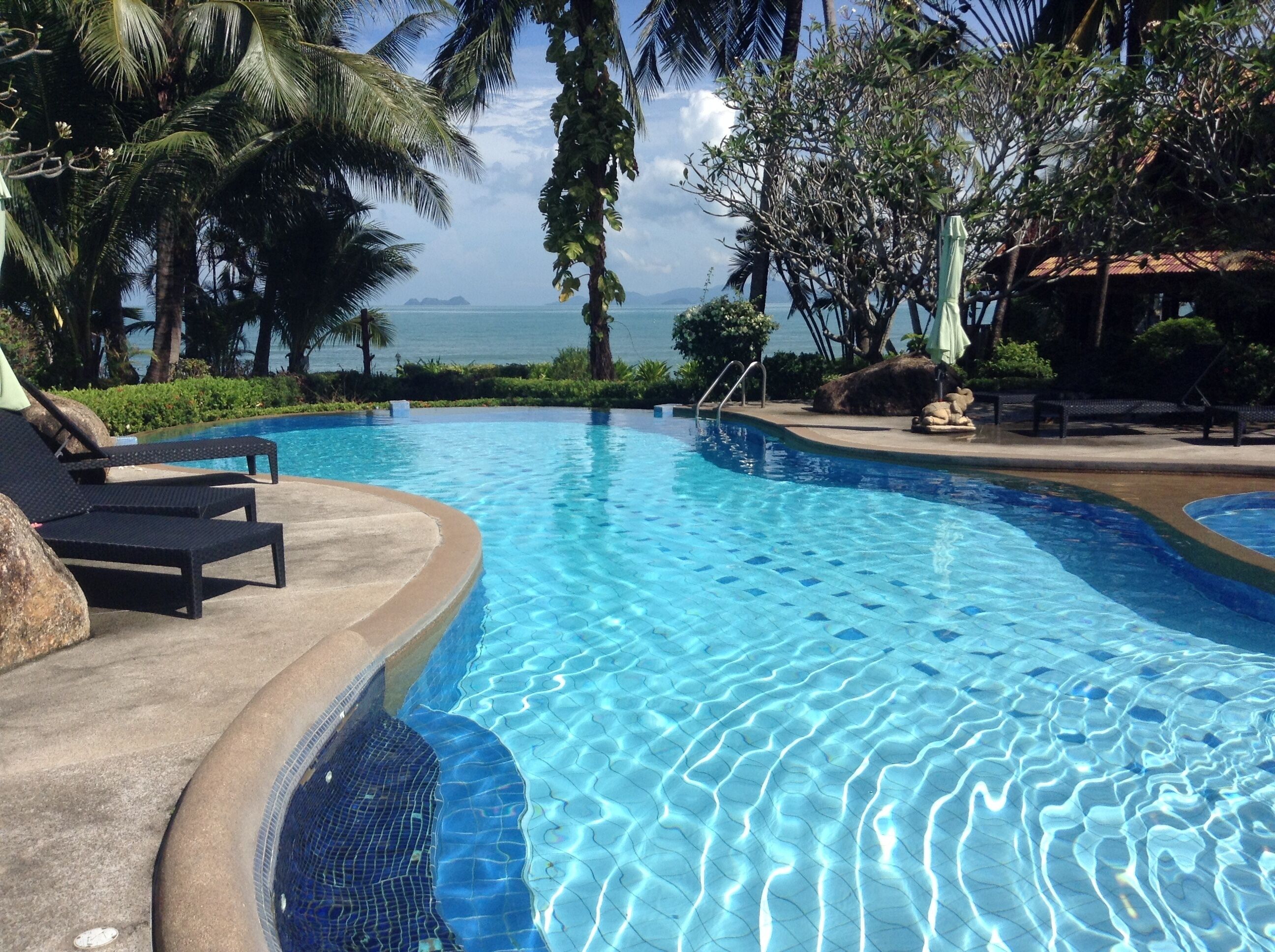 En swimmingpool med solstolar och utsikt över havet.