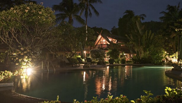 A nighttime resort with a swimming pool, palm trees, and a lit-up building.