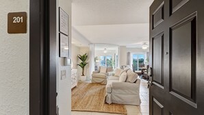 Un moderno salón con un sofá beige, una planta grande y vistas al exterior.