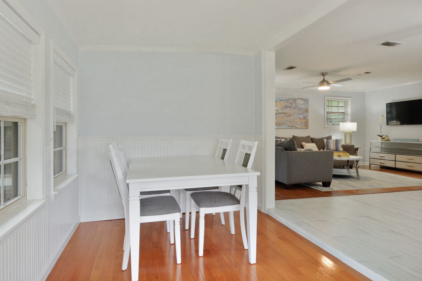 A dining area with a white table and chairs, a grey sofa, and a TV in the background.