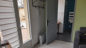 Une pièce avec une porte donnant sur un balcon, un radiateur, un bureau avec une chaise et un canapé gris.