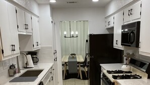A modern kitchen with white cabinets, a dining table with chairs, and a black refrigerator.