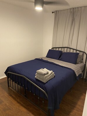 A single bed with a metal frame, dark blue bedding, and a folded white towel on the footboard.