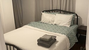 A single bed with a white and green patterned bedspread, a black metal frame, and a small bedside table.