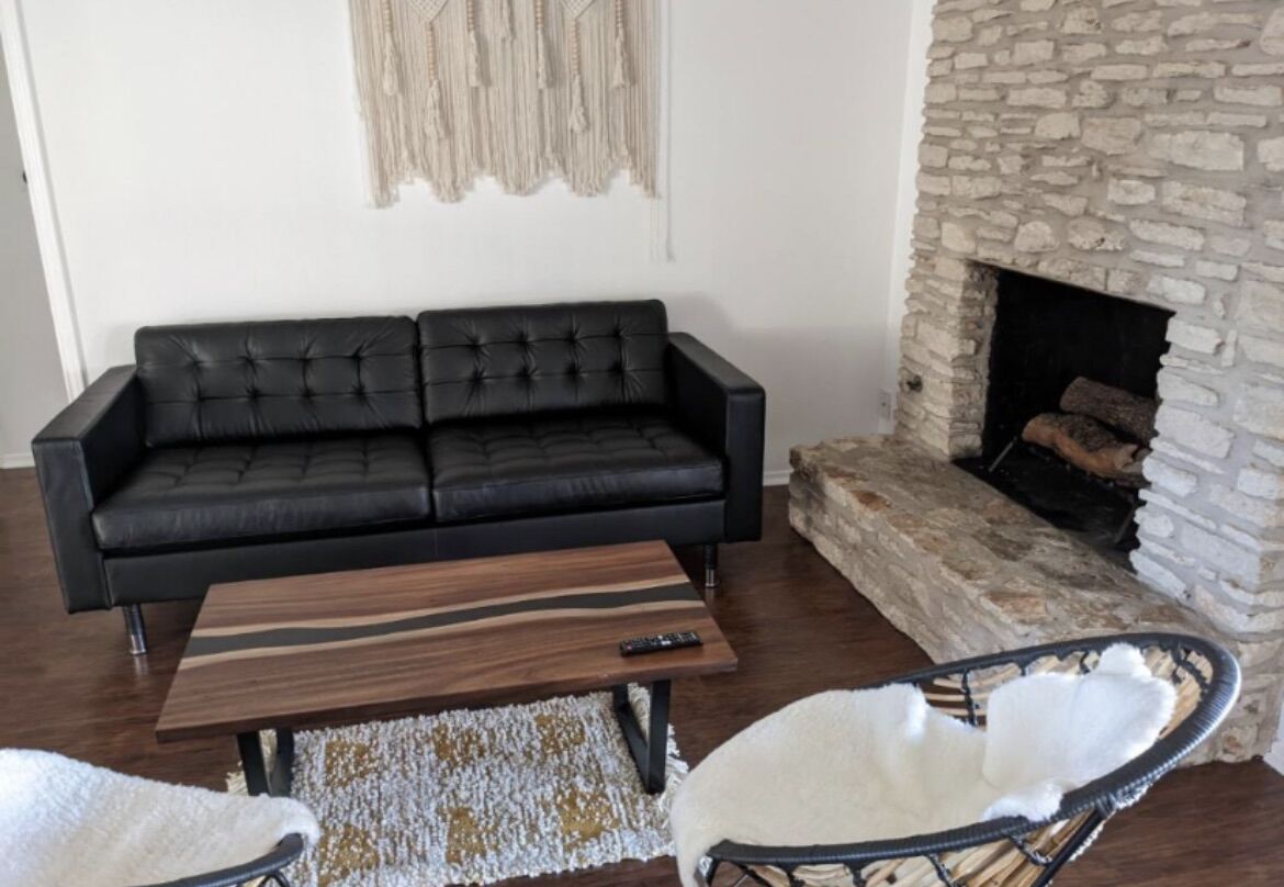 A living room with a black leather sofa, a wooden coffee table, a white chair, and a stone fireplace.