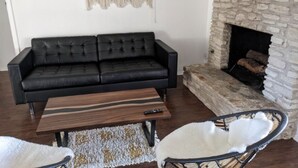 A living room with a black leather sofa, a wooden coffee table, a white chair, and a stone fireplace.