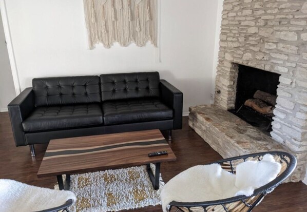 A living room with a black leather sofa, a wooden coffee table, a white chair, and a stone fireplace.