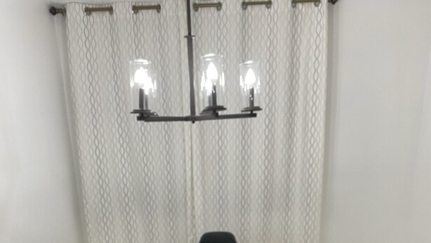 A dining table with a grey runner, black chairs, and a chandelier with four lights.