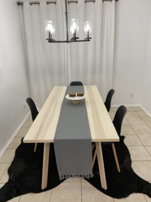 A dining table with a grey runner, black chairs, and a chandelier with four lights.