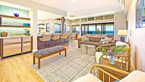 A spacious living area with a large window, a kitchen with a bar, and a balcony with a view.