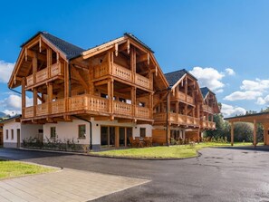 A multi-story wooden chalet with balconies, a covered outdoor seating area, and a paved driveway.