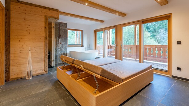 A modern bedroom with a large bed, a bathtub, and a sliding glass door leading to a balcony. - Very luxurious apartment with sauna (Mauterndorf)