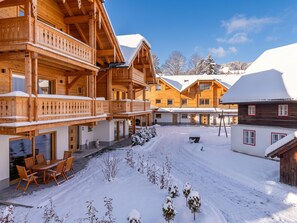 A wooden chalet with a covered outdoor seating area and a snow-covered courtyard. - Exquisite apartment with private sauna (Mauterndorf)