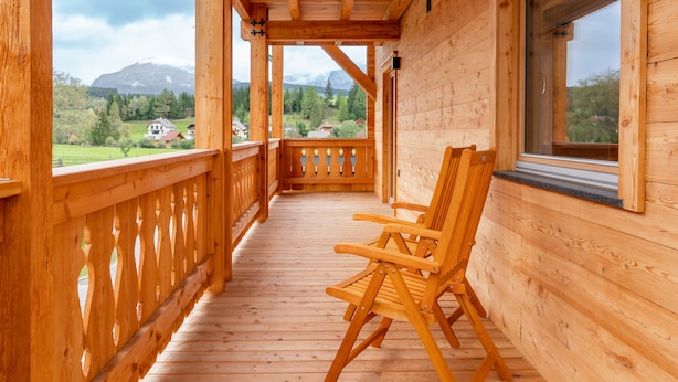 A wooden deck with two wooden chairs, a wooden railing, and a window overlooking a mountainous landscape. - Comfortable apartment with sauna (Mauterndorf)