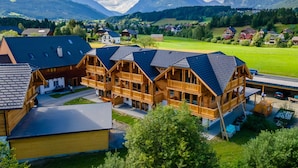 A wooden chalet-style building with a sloped roof, surrounded by a green landscape and mountains in the background. - Comfortable apartment with sauna (Mauterndorf)