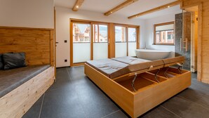 A modern bedroom with a wooden bed, a large window, and a bathroom with a bathtub. - Comfortable apartment with sauna (Mauterndorf)