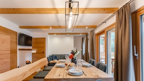 A modern dining area with a long wooden table, cushioned benches, and a fireplace. - Comfortable apartment with sauna (Mauterndorf)