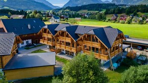 Un bâtiment de style chalet en bois, doté de plusieurs balcons, d’un espace de stationnement et offrant une vue sur les montagnes et les champs environnants.