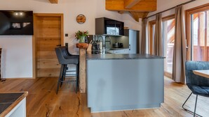 Une cuisine moderne avec un îlot central, des poutres en bois et une grande fenêtre.