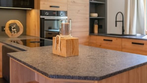 A modern kitchen with wooden cabinets, a granite countertop, and a glass candle holder. - Exclusive apartment with private sauna (Mauterndorf)