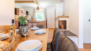 A dining area with a wooden table set for four, a vase of flowers, and a fireplace in the background. - Exclusive apartment with private sauna (Mauterndorf)