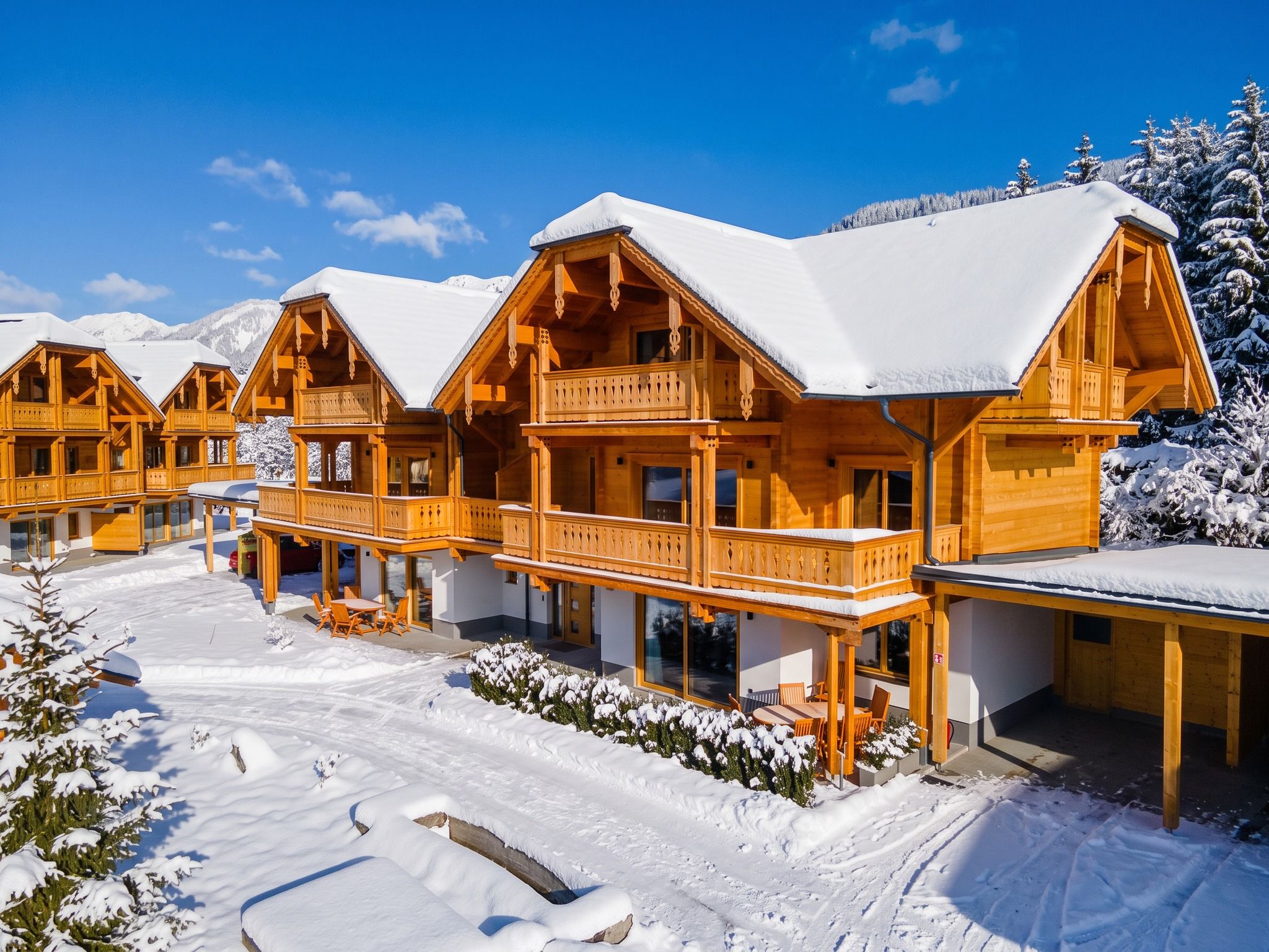 Un hôtel de style chalet en bois, doté de nombreux balcons, entouré d’arbres couverts de neige et surplombant un ciel bleu azur.