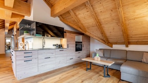 Loft moderno con travi a vista in legno, cucina con forno integrato e divano grigio.