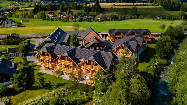 Un'ampia struttura in legno con numerose camere, un cortile centrale e vista sulle montagne e i campi circostanti.