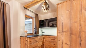Eine kleine Küche mit Holzschränken, einem schwarzen Wasserhahn und einem Fenster mit Vorhängen.