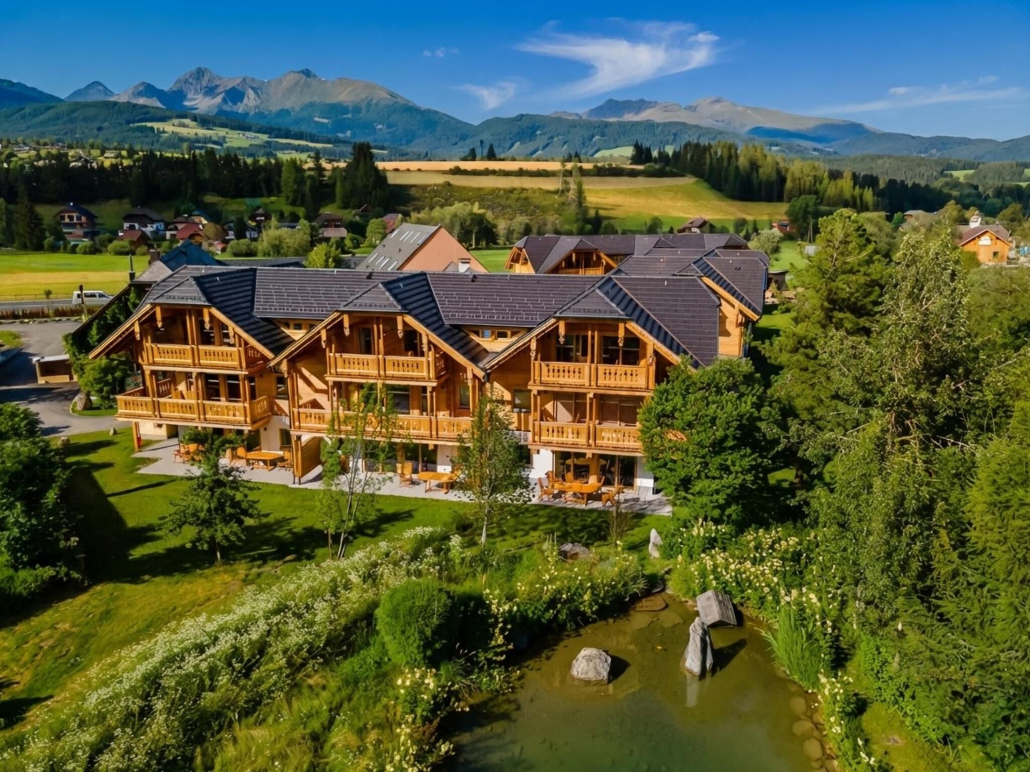 Un grand chalet en bois doté de nombreux balcons et d’un étang en premier plan.