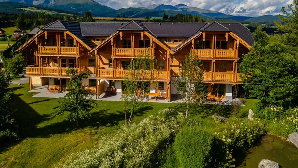 A wooden chalet with multiple balconies, surrounded by lush greenery and mountains in the background. - Luxuriously furnished penthouse (Mauterndorf)