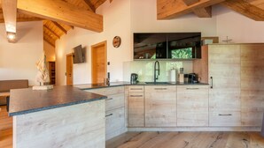 A modern kitchen with wooden beams, a built-in island, and a large window. - Luxuriously furnished penthouse (Mauterndorf)