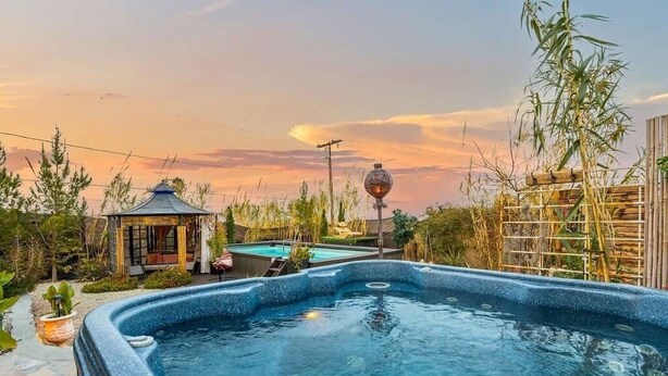 Una vasca idromassaggio circondata da un giardino con un gazebo e una piscina.