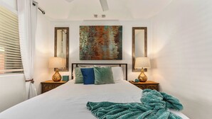 Un letto rifatto con cura, una coperta verde, due abat-jour e un grande quadro astratto sopra il letto.