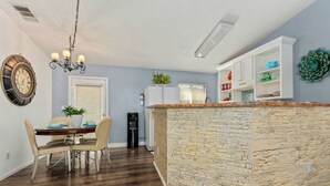 Una cucina moderna con isola centrale, pavimento in legno, zona pranzo con tavolo e sedie e un orologio decorativo a parete.