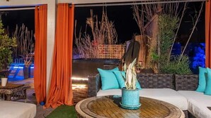 Zona esterna con posti a sedere, un tavolo rotondo, cuscini e una pianta in vaso.