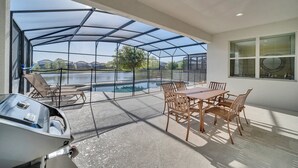 Een overdekt terras met een zwembad, tuinmeubels en een barbecue.