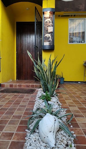 Welcome to a tranquil entrance, featuring a vibrant exterior wall, a dark door, and a decorative dolphin sculpture amidst a colorful stone display.