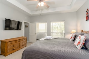 A bedroom with a bed, dresser, ceiling fan, TV, and windows.