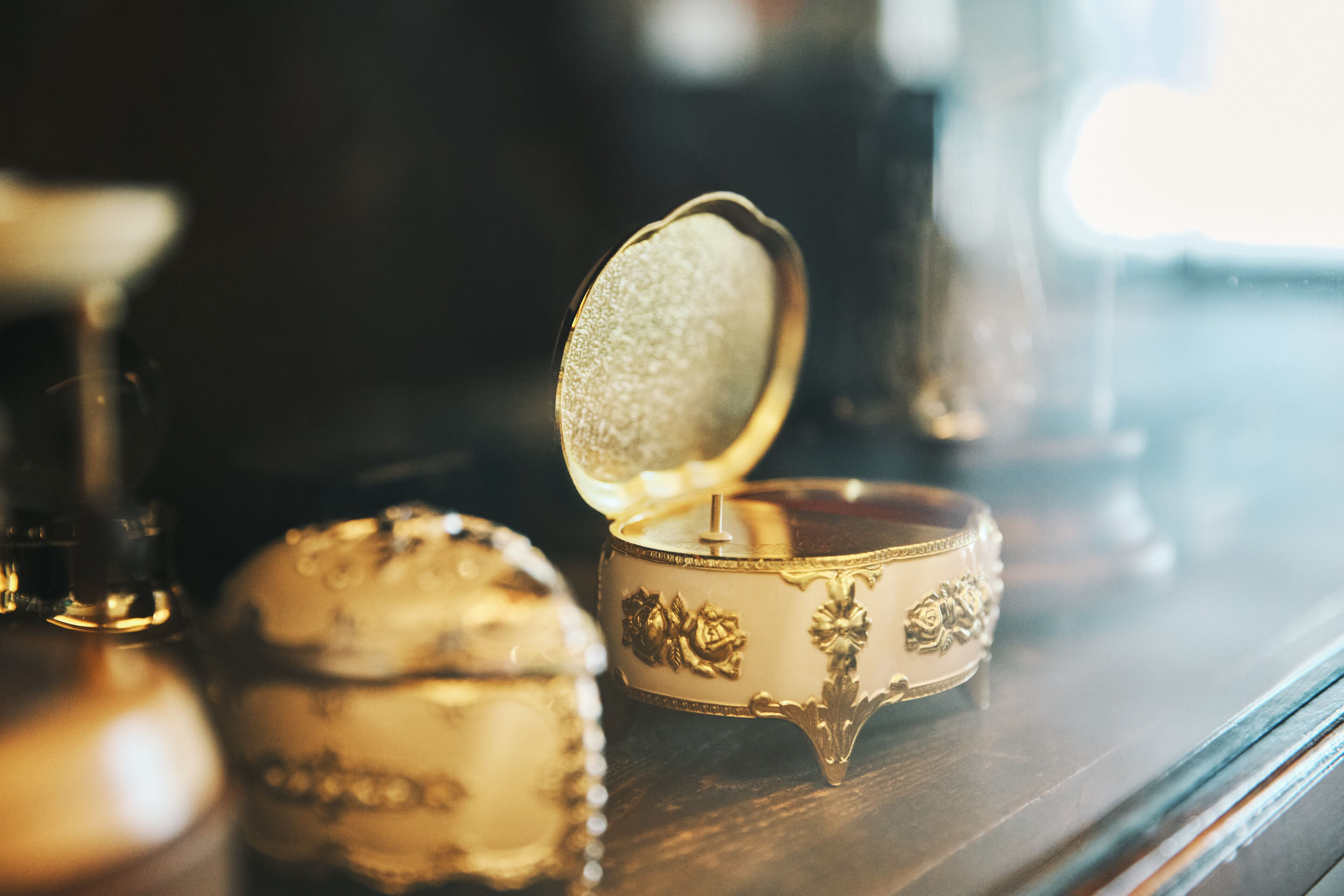 A gold-colored jewelry box with a lid open, revealing a reflective interior.