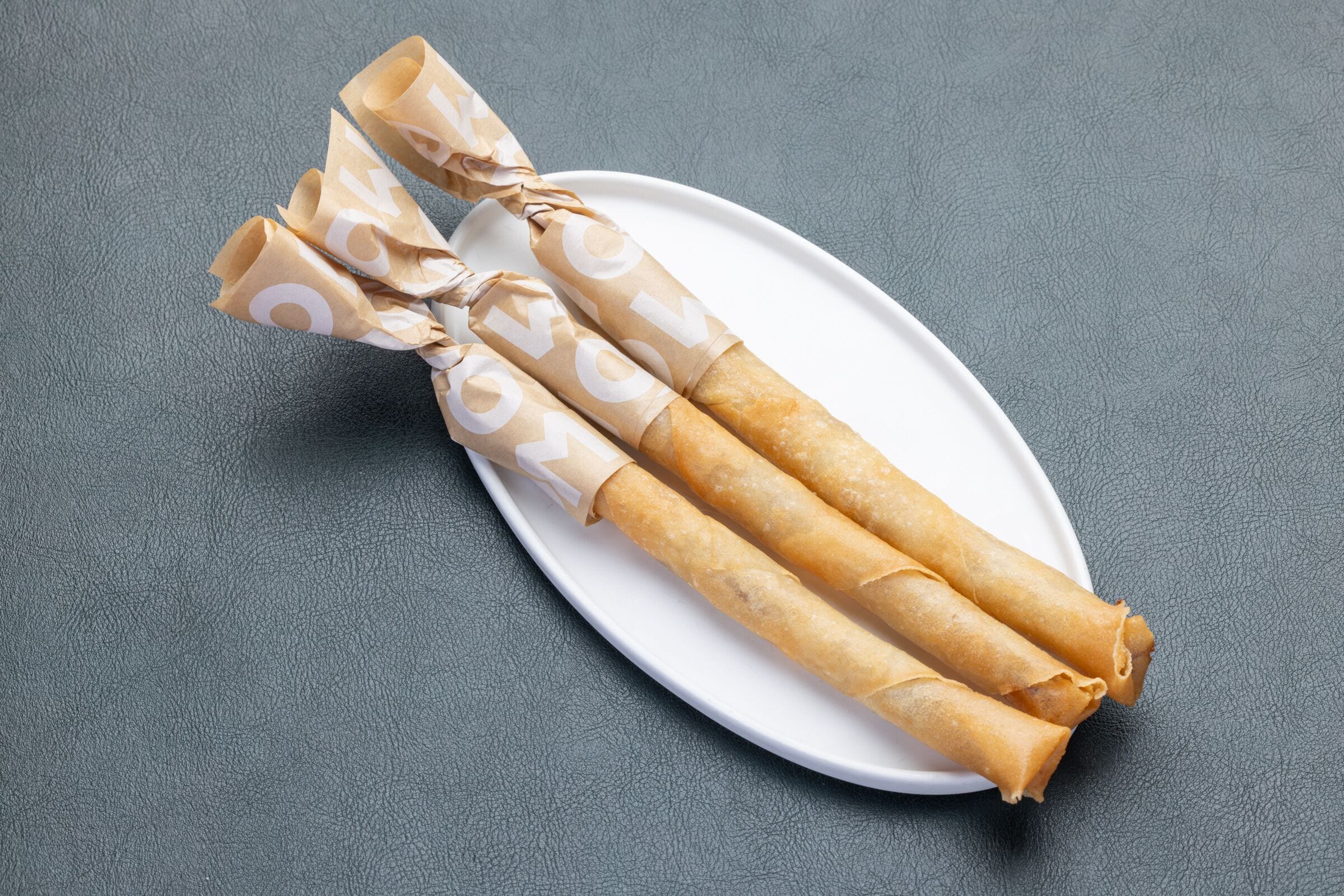 A plate with three spring rolls wrapped in paper with the word "LOVE" printed on it.