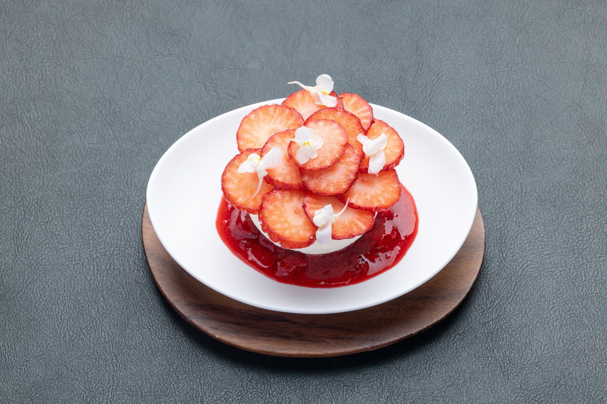 A dessert on a white plate with a red sauce, placed on a wooden board.