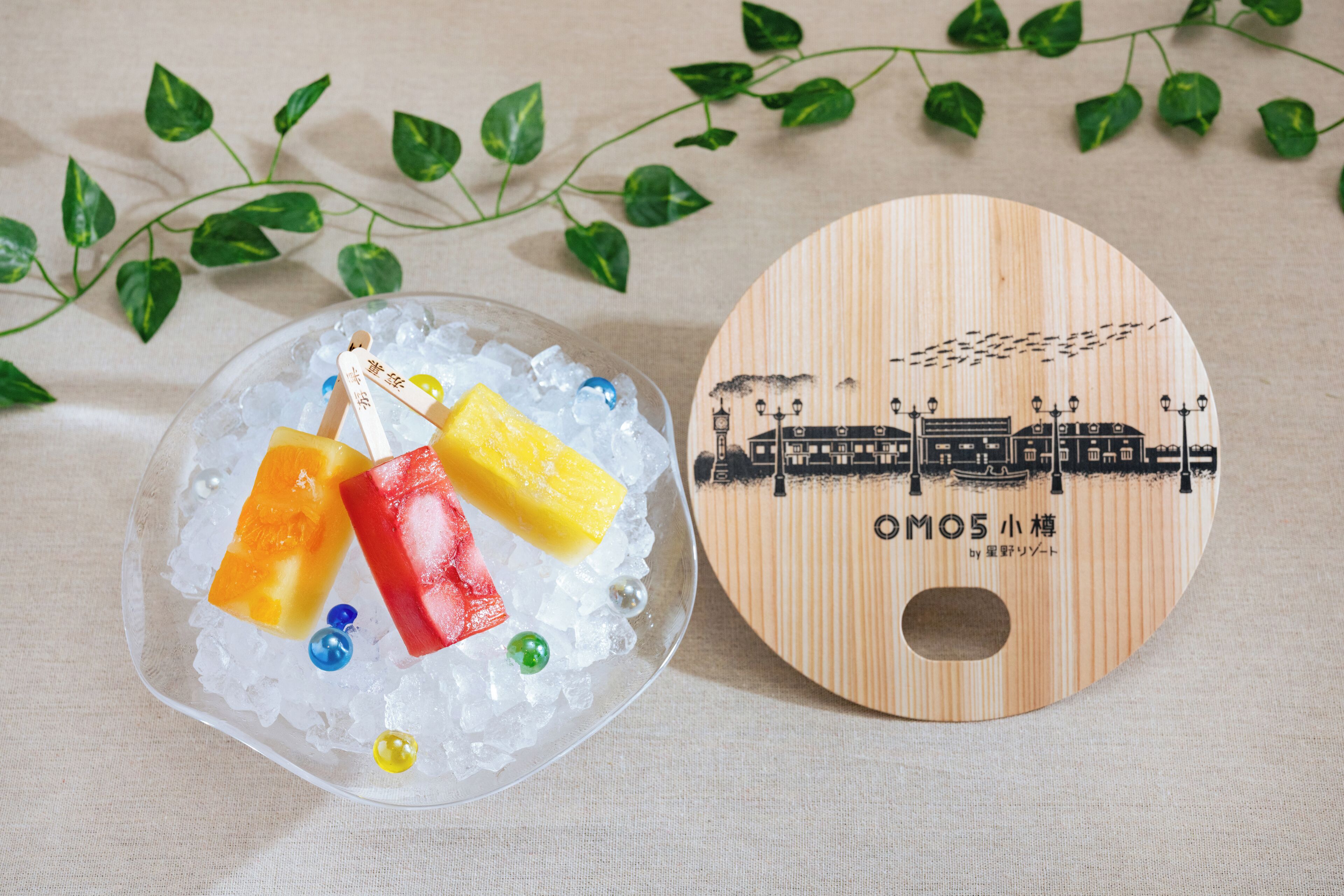 Una placa de madera con una ilustración de tren y texto, junto a un recipiente de vidrio con hielo y objetos coloridos.