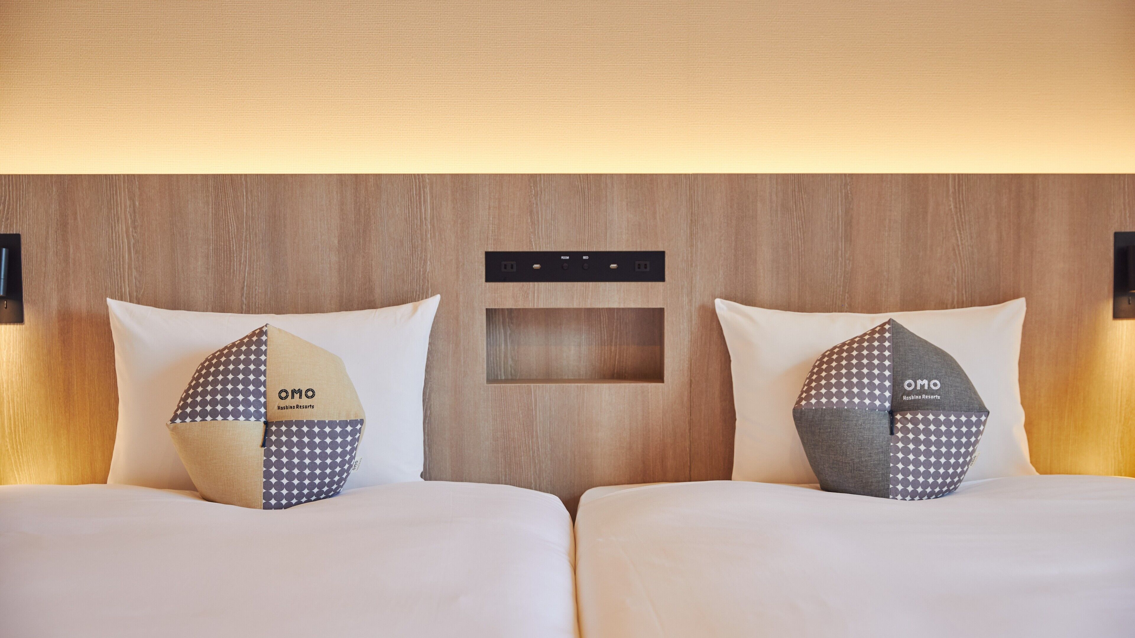 Een hotelkamer met twee bedden, elk voorzien van een kussen met een geometrisch patroon en het logo "OMO".