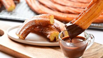 A plate of churros with chocolate sauce being poured over them.